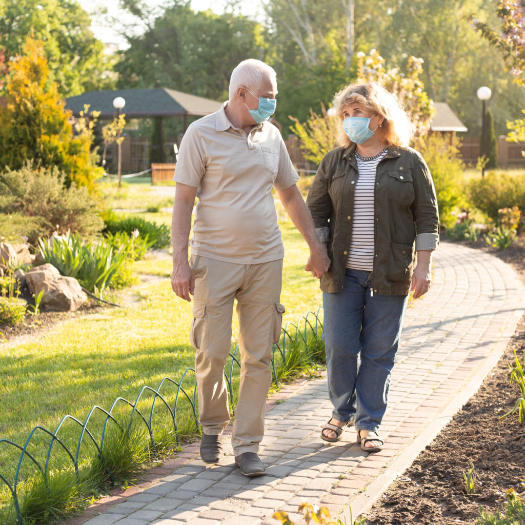 older man and woman holding hands and talking with masks on
